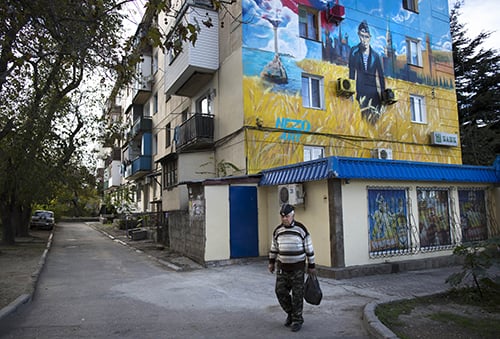 In this photo taken on Sunday, Oct.  26, 2014, a man in Russian Navy hat walks past a mural on an apartment building depicting Russian President Vladimir Putin in a navy uniform with the Kremlin and a Russian flag in the background in Sevastopol,  Crimea. Russia on Saturday dismissed new U.S. sanctions as useless and said it was poised to wait as long as it takes for the U.S. to recognize its historic right to the Crimean peninsula. Following several rounds of sanctions earlier this year, President Barack Obama on Friday approved new restrictions on Crimea which Russia annexed in March after a hastily called referendum.(AP Photo/Alexander Zemlianichenko)