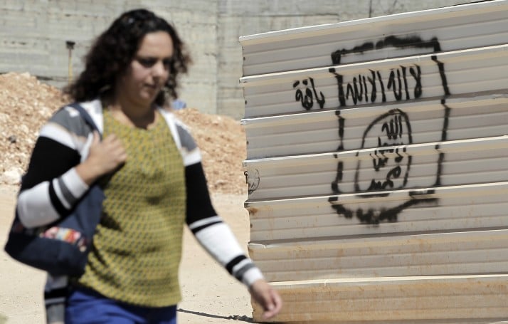 A woman walks past a graffiti portraying the Islamic State (IS) group's flag in the East Jerusalem neighbourhood of Beit Hanina on July 5, 2015. AFP PHOTO / AHMAD GHARABLI (Photo credit should read AHMAD GHARABLI/AFP/Getty Images)