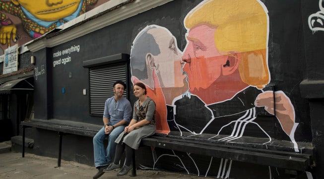 A couple sits in front of graffiti depicting Russian President Vladimir Putin, left, and Republican presidential candidate Donald Trump, on the walls of a bar in the old town in Vilnius, Lithuania, Saturday, May 14, 2016. (AP Photo/Mindaugas Kulbis)
