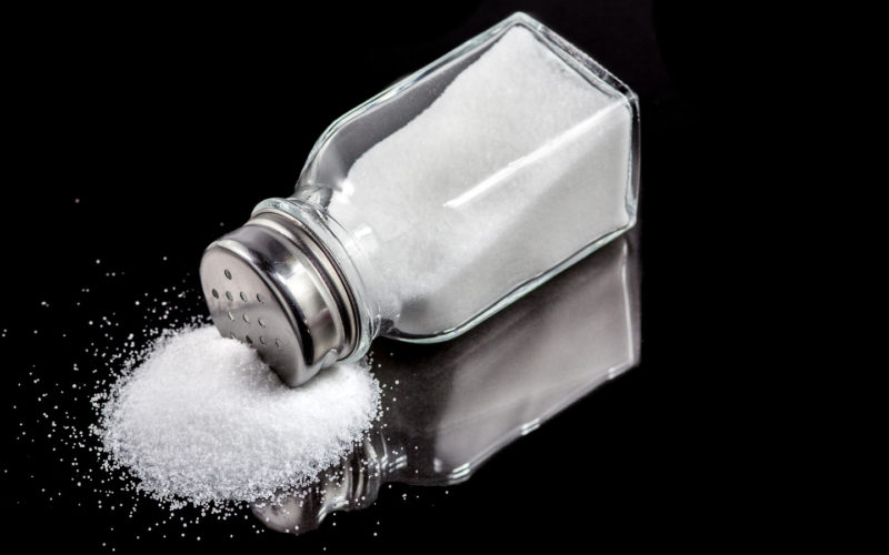 Salt,Shaker,With,Spilled,Salt,On,A,Black,Background